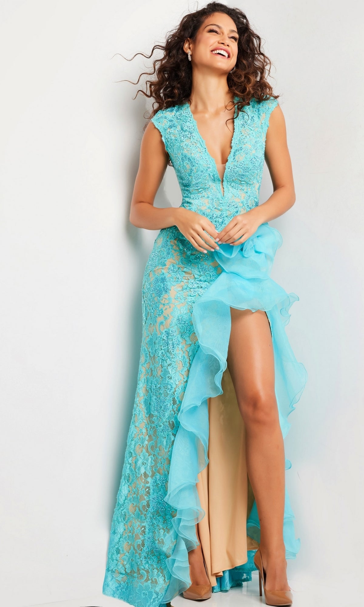 A woman models the Jovani Ruffled Long Lace Prom Dress 38668, featuring a sleeveless turquoise beaded lace design with a deep V-neckline and ruffled high slit, set against a plain light-colored background.